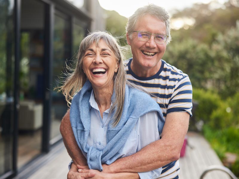Mature couple standing arm in arm and laughing outside in summer