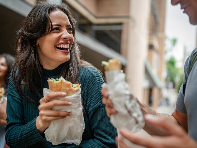 Woman laughs while holding a sandwich and socializing
