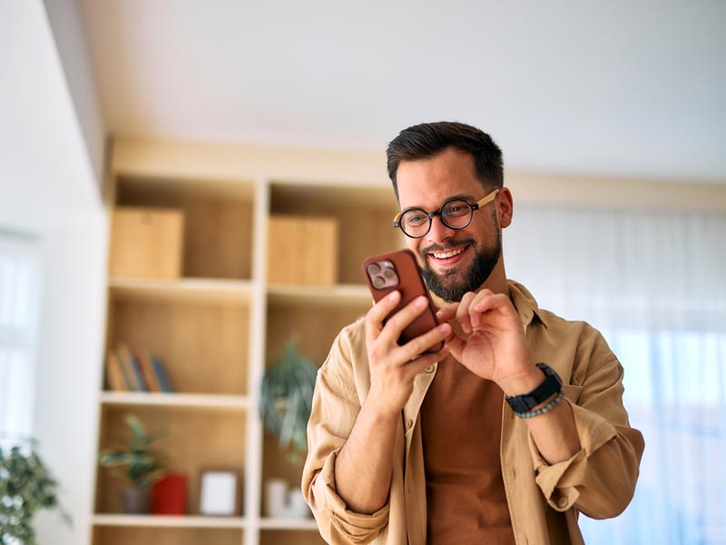 Young man using smartphone at home, smiling and looking at screen